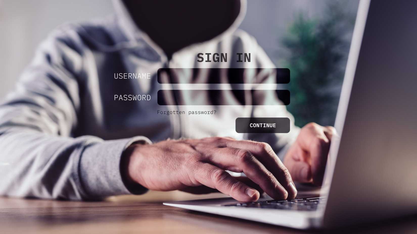 A dark hooded figure ominously using a laptop. 