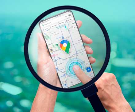 A magnifying glass showing a smartphone with Google Maps open and a person's finger pointing towards the screen.